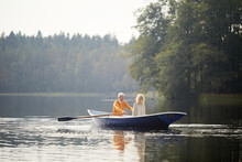 Happy Senior Couple In Casual Clothing Sitting On Boat And Enjoying Romantic Date On Lake, Elderly Man Rowing Oars