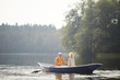 Excited handsome senior boyfriend in yellow sweater sitting on boat with beloved woman and rowing oars at date on lake