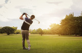 Golfer hitting golf shot with club on course at evening time.