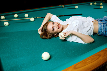 Young woman lying on the billiard table and looking at camera.