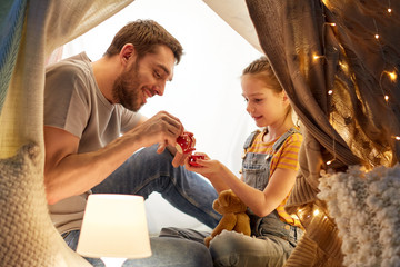 Wall Mural - family, hygge and people concept - happy father and little daughter playing tea party in kids tent at night at home