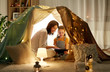 © Syda Productions - family, hygge and technology concept - happy mother and little daughter with tablet pc computer in kids tent at night at home