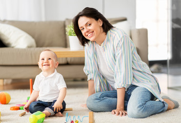 Wall Mural - family, child and motherhood concept - happy mother with little baby son playing developmental toys at home