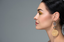side view of young brunette woman with beautiful earring looking away isolated on grey