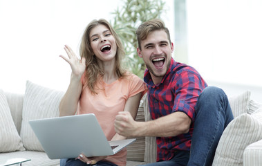 Poster - young couple rejoices,sitting on the couch in front of the open laptop