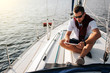 © estradaanton - Serious and peaceful guy sits on board of yacht. He holds and looks at tablet. Young man is calm. He wears white sirt and dark sweater with shorts.