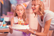 © zinkevych - Blowing candles. Kind loving mother smiling and holding big cake while her daughter blowing candles and making a wish