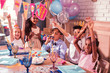 © zinkevych - Hands up. Relaxed cheerful kids sitting at the party table and putting hands up while having fun