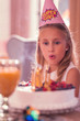 © zinkevych - Impressing cake. Pretty little girl wearing party hat and blowing candles on her amazing cake while having birthday party