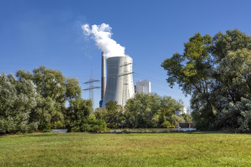 Big power plant with white exhaust gases steam, green trees, grass field, skyline and blue sky in background - concept electricity power business technology consumption nature environmental pollution