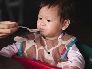 Asian toddler with dirty bib eat meal  by mom feed.