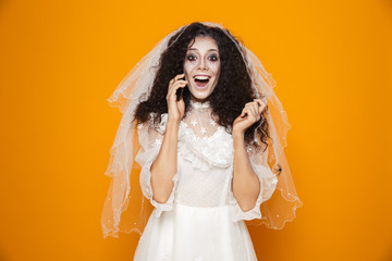 Poster - Image of european zombie woman on halloween wearing wedding dress and scary makeup talking on cell phone, isolated over yellow background