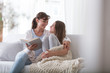 Happy mother reading book to smiling daughter while relaxing at home