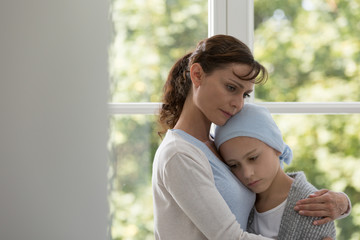 Wall Mural - Sad mother hugging sick daughter with cancer wearing blue headscarf