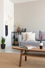 Wall Mural - Flowers on wooden table in front of grey settee in simple living room interior with plant. Real photo