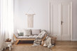 Pillows and blanket on wooden sofa in white loft interior with door and table on carpet. Real photo