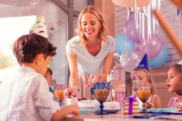 Piece of cake. Cheerful young woman smiling and giving piece of cake to the boy at birthday party