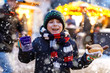 Little cute kid boy eating German sausage and drinking hot children punch on Christmas market