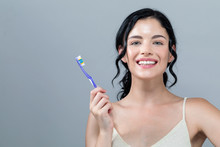 Young Woman Holding A Toothbrush On A Gray Background