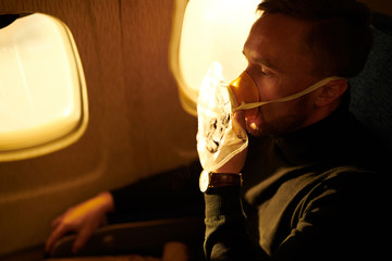 Wall Mural - Side view portrait of mature man wearing oxygen mask in plane, copy space