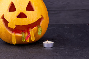 Halloween pumpkin with candle on dark background. Funny carved pumpkin and burning candle on black background. Happy Halloween Day.