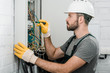 © LIGHTFIELD STUDIOS - side view of handsome bearded electrician repairing electrical box and using screwdriver in corridor