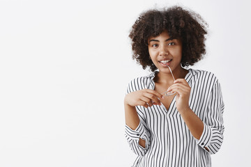 Wall Mural - indoor shot of playful attractive dark-skinned woman with afro hairstyle biting rim of glasses and s
