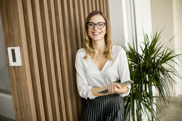 Wall Mural - Young businesswoman with digital tablet by the wall in modern office