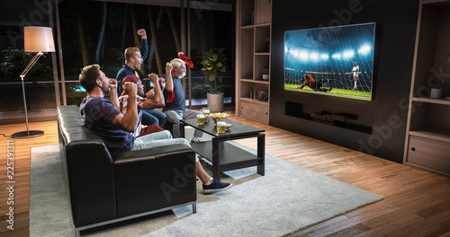 Cuadros en Lienzo Group of fans are watching a soccer moment on the TV and celebrating a goal, sitting on the couch in the living room