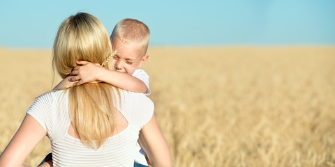 a small son gently hugs his mother in a wheat field.