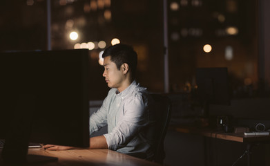 Canvas Print - Young Asian businessman sitting at his workstation late at night