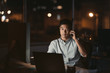 © mavoimages - Asian businessman talking on a cellphone in a dark office