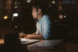 © mavoimages - Young Asian businessman working online in a dark office