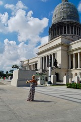 Beautiful blonde Caucasian (European) female tourist taking a photo in front of the Capitol (Capitolo) in Havana (Cuba, Caribbean island) on a sunny day