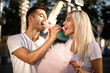 © Sunrise Team - Happy young cheerful loving couple walking outdoors in the amusement park posing eat sweeties cotton candy floss.