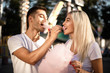 © Sunrise Team - Happy young cheerful loving couple walking outdoors in the amusement park posing eat sweeties cotton candy floss.