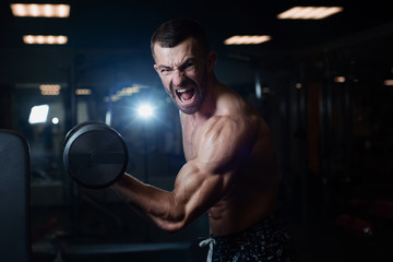 young muscular man exercising with dumbbells. Guy trains his bicep