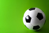Fototapeta Sport - Sports equipment and leisure activity concept with a black and white generic classic leather football or soccer ball isolated on green background with copy space