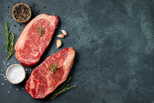 Fresh Raw Prime Black Angus Beef Steaks On Stone Board: Striploin, Rib Eye. Top View With Copy Space. On A Dark Background
