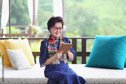 Photographie asian senior woman sitting on the sofa and using a tablet