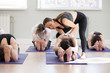 © fizkes - Young female yoga instructor teaching paschimottanasana pose, Seated forward bend exercise for a group of sporty people practicing in studio, working out indoor, teacher helping to master, full length