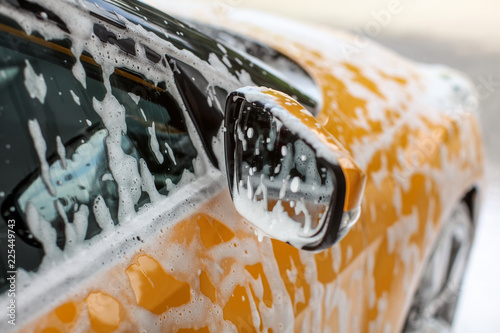 Fotografia, Obraz Detail on yellow car side mirror, covered with shampoo and foam spots, when washed in carwash