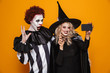Happy witch and clown making selfie on smartphone isolated