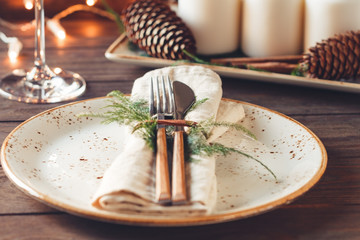 Thanksgiving table setting among white candles and cones. Ceramic plate with fork and knife on a linen napkin. The concept of a festive dinner.