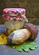 Marinated Boletus edulis mushrooms in a glass jar with fresh Porcini mushroom on old wooden table.
Selective focus.