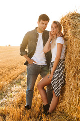 Wall Mural - Full length photo of young couple man and woman walking on field, and standing near big haystack