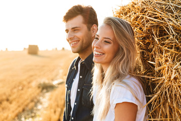 Image of lovely people man and woman walking on golden field, and standing near big haystack