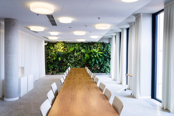 Living green wall, vertical garden indoors with flowers and plants under artificial lighting in meeting boardroom, modern office building