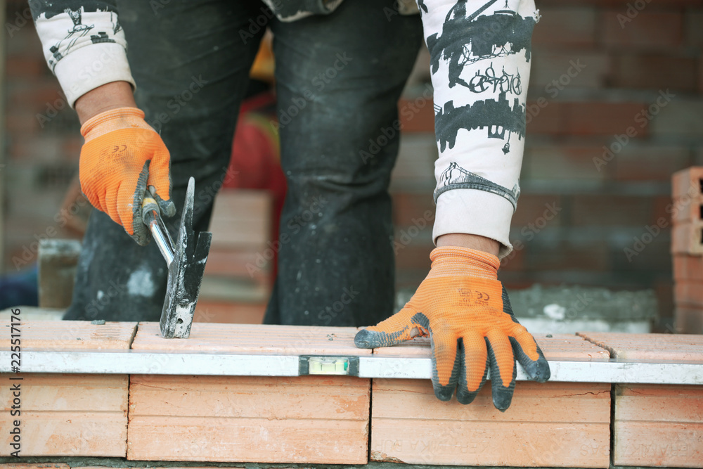 Industrial bricklayer installing bricks on construction site. - obrazy, fototapety, plakaty 
