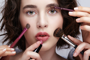 Make-up artist apply beauty makeup on the face of a beautiful girl. Visagist with makeup brush in hand